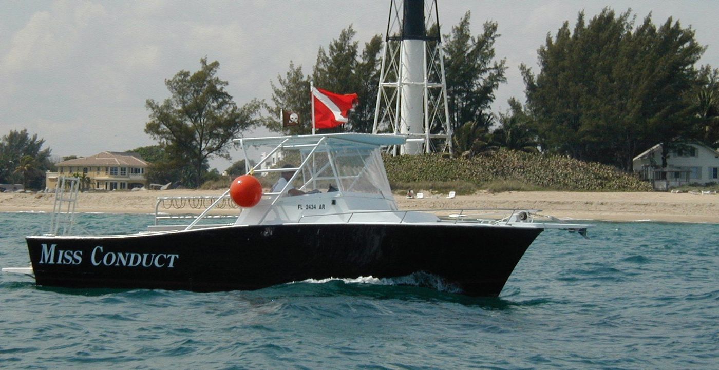 The Miss Conduct, a black 30-foot dive boat flying a dive flag, off the beach at the Hillsboro Inlet lighthouse